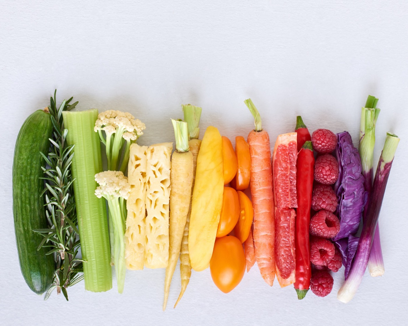 Légumes, herbes et fruits alignés en dégradé, du concombre vert à l’oignon rouge.
