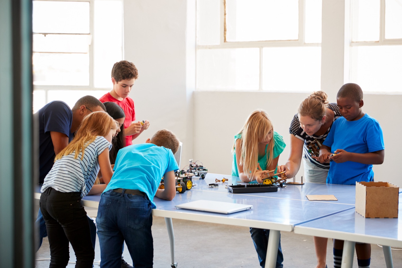 Des élèves assemblent de petits robots autour de tables, accompagnés d'adultes, dans une salle lumineuse.