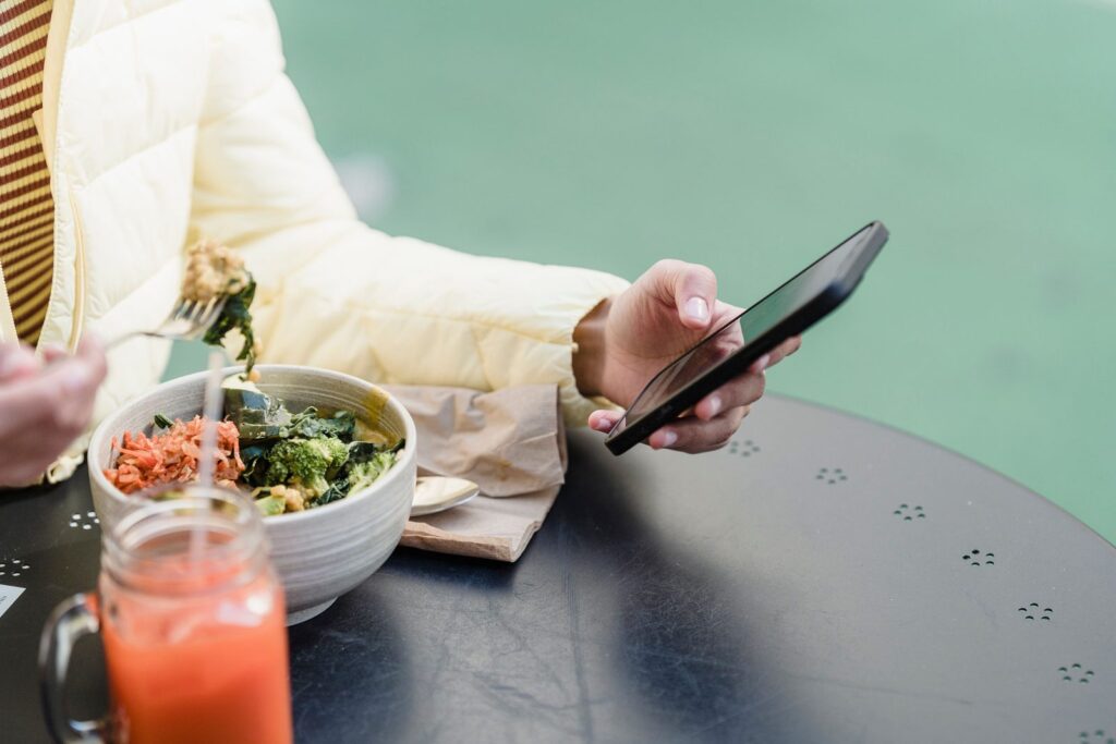 Une main tient un téléphone au-dessus d'un bol de crudités et d'un verre de jus.
