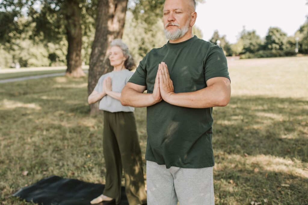 Deux personnes debout dans un parc, mains jointes devant la poitrine, pratiquent la méditation.
