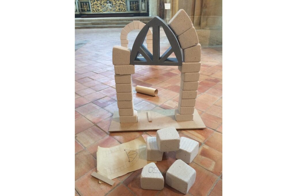 Une maquette d'arc en blocs de pierre reconstituée sur le sol, à côté des blocs restants.