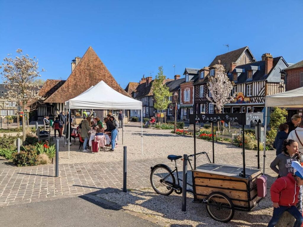 Des stands sous barnum installés sur la place d'un village normand à colombages.