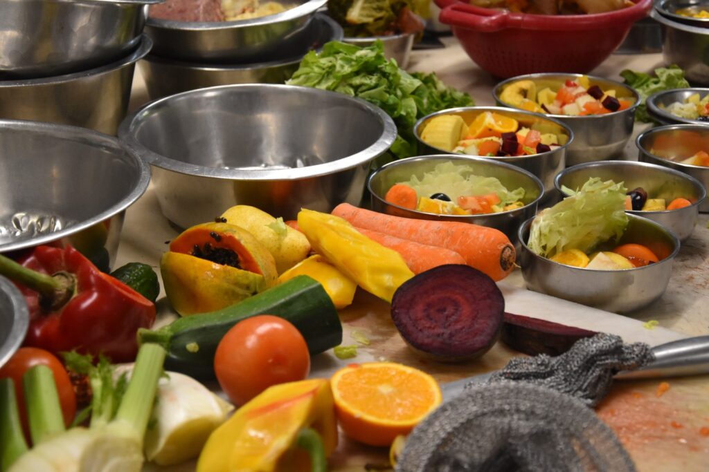 Légumes crus et préparations dans des bols en inox disposés sur un plan de travail.