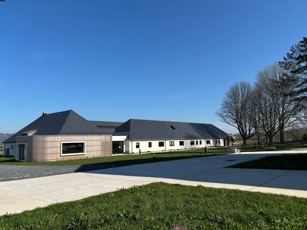 Bâtiment bas aux façades de bois clair, entouré de pelouse.