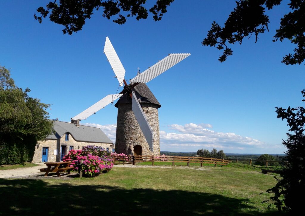 Moulin à vent en pierre aux ailes déployées, dans un jardin fleuri.