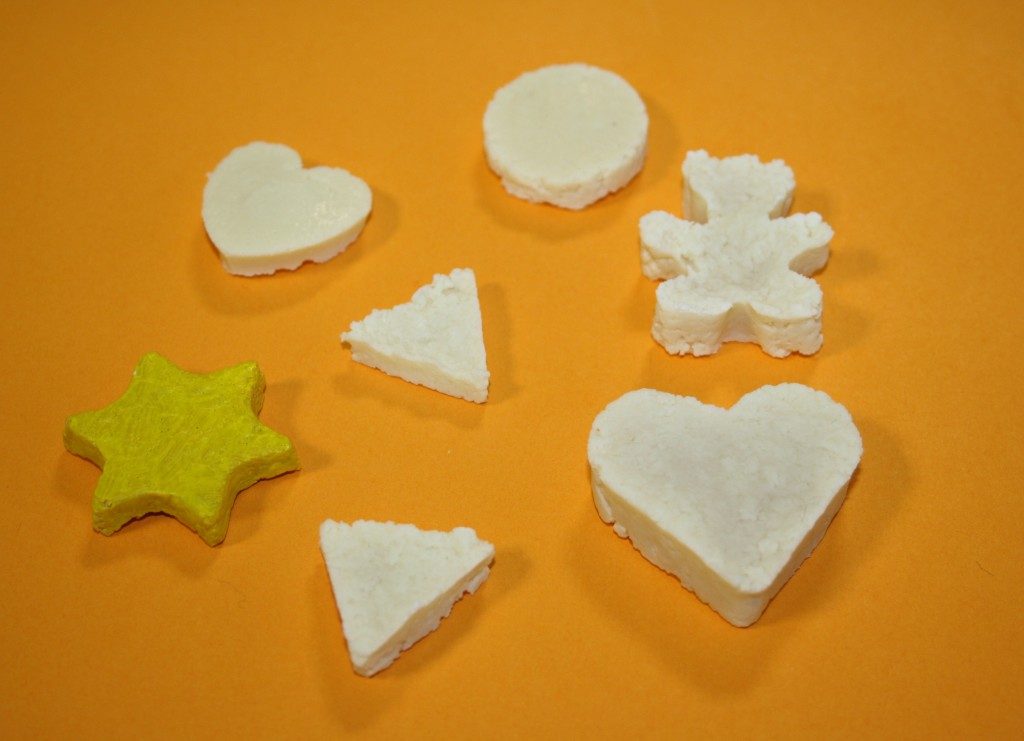 Petites pièces blanches en forme de cœur et d'étoile moulées dans de la caséine, sur fond orange.