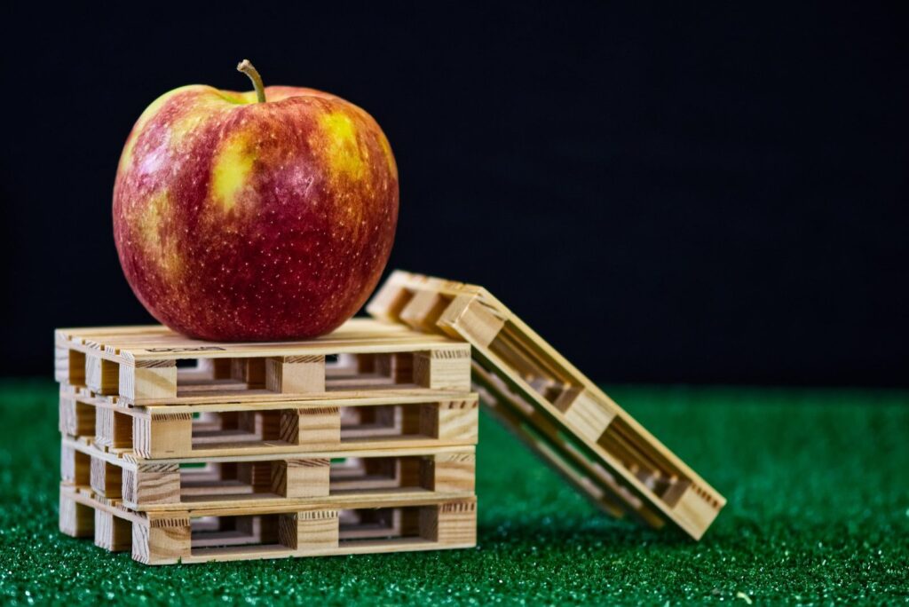 Une pomme rouge posée au sommet de palettes de bois empilées en équilibre.