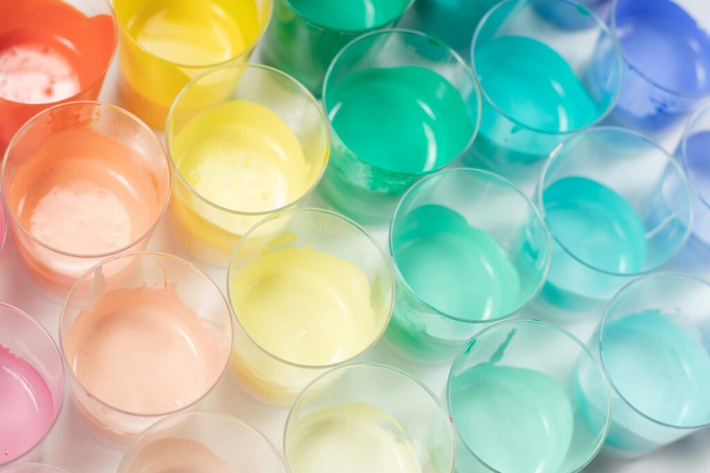 Gobelets transparents remplis de liquides roses, jaunes, verts et bleus, vus de dessus.