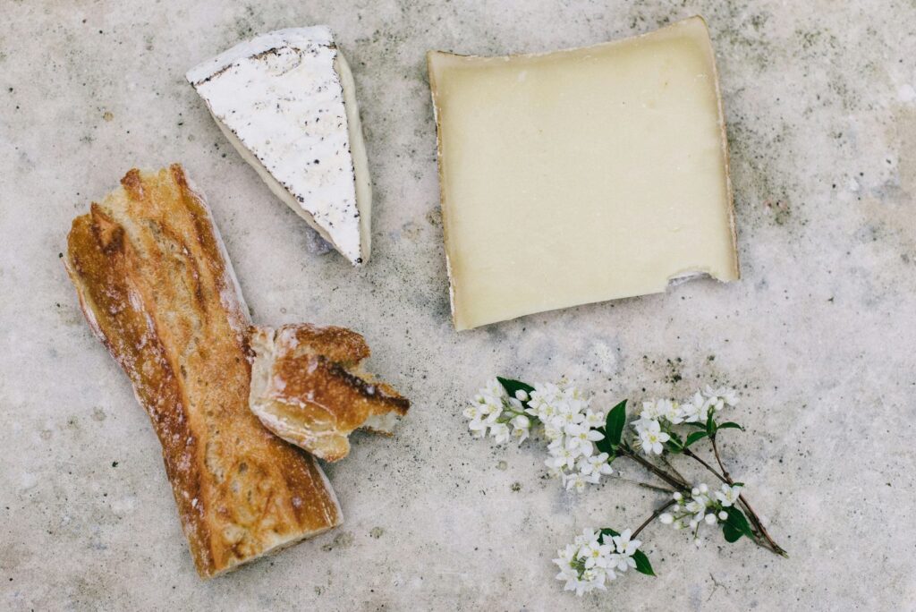 Morceaux de fromages et tranche de pain disposés sur une pierre claire, avec des fleurs de prunier.