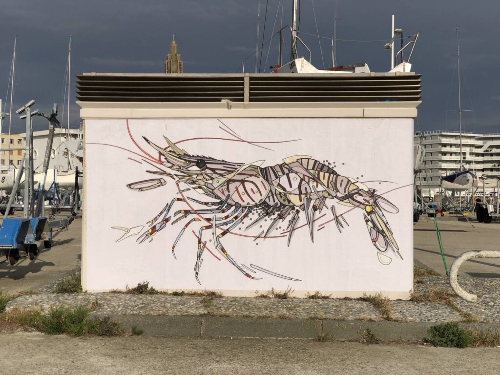 Grande fresque murale représentant une crevette, peinte sur un bâtiment au bord d'un port.