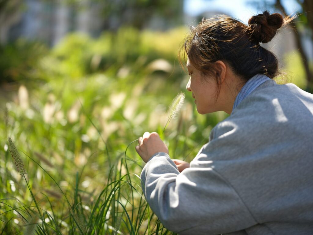 Une personne se penche pour sentir des graminées dans un champ.