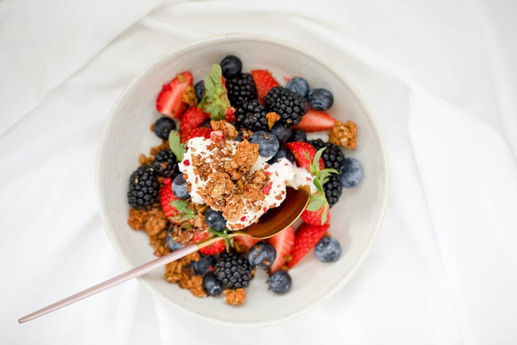 Bol de fromage blanc garni de fraises, de mûres, de myrtilles et de granola, vu de dessus.