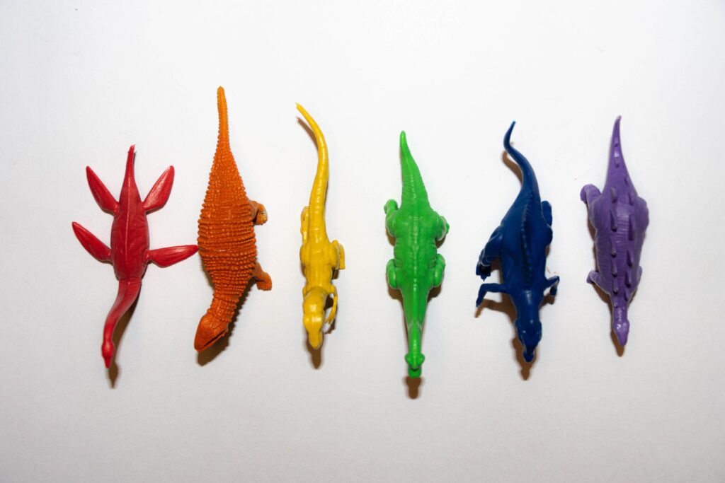 Six figurines de dinosaures en plastique alignées par couleur sur un fond blanc.