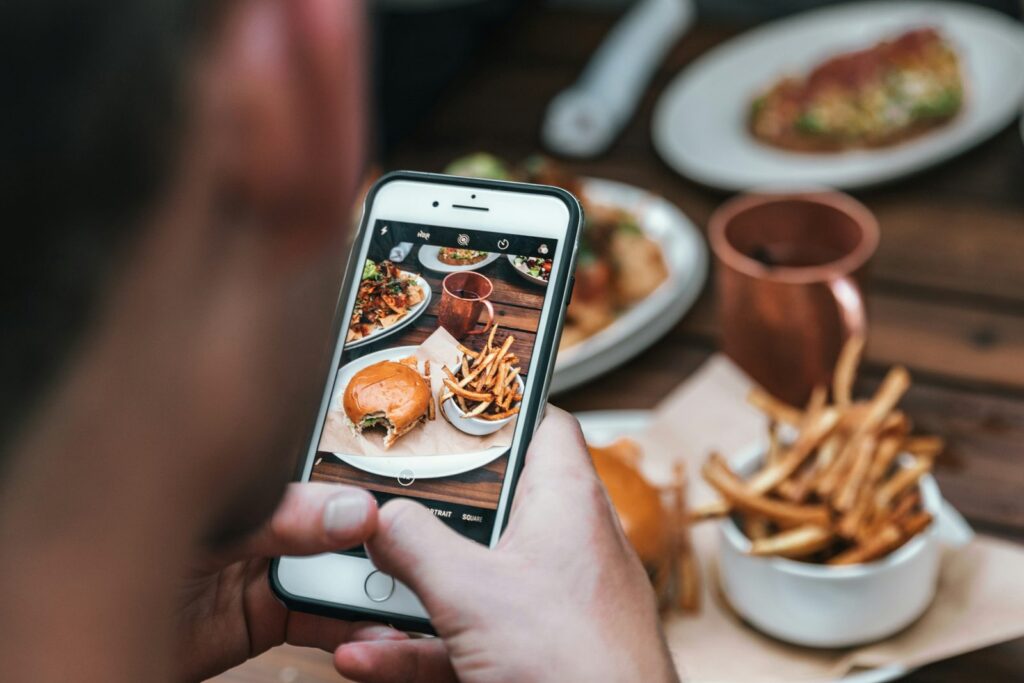 Une main photographie avec un téléphone une assiette de burger et de frites.