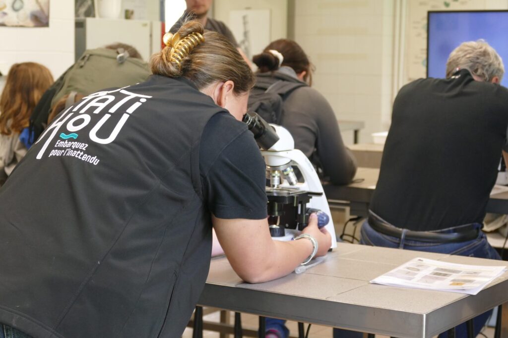 Des personnes observent des échantillons au microscope autour d'une table, dans une salle d'atelier.
