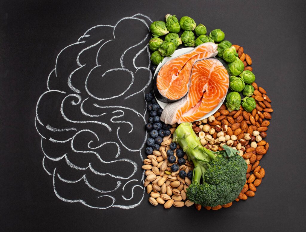 Un cerveau dessiné à la craie sur un tableau noir, dont une moitié est remplie de saumon, de brocolis et de fruits secs.