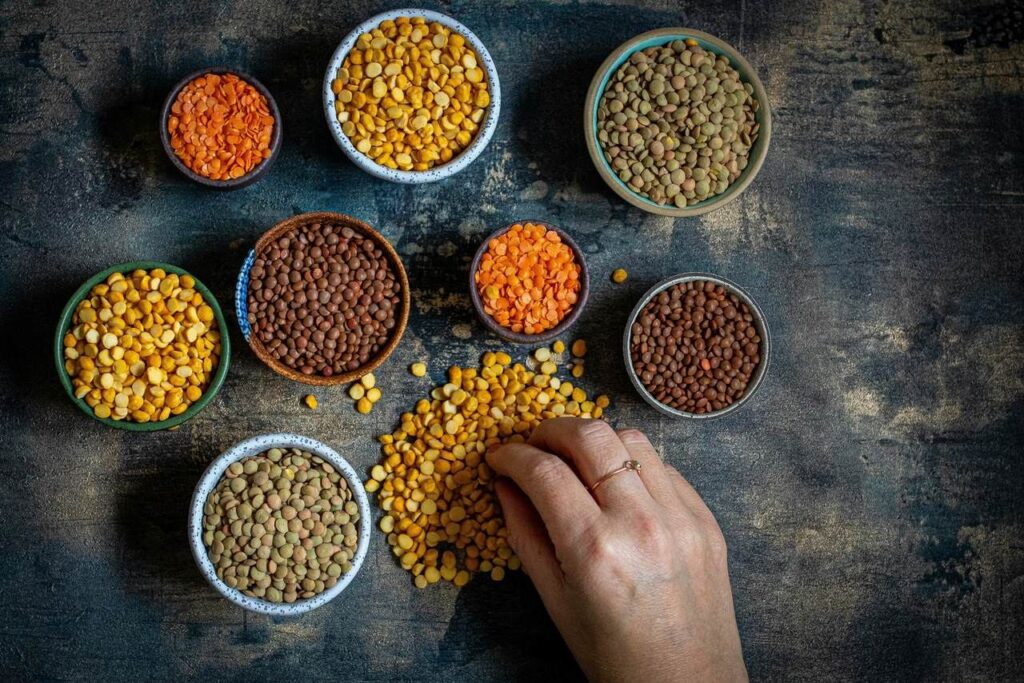 Bols de lentilles, de pois et de pois chiches vus de dessus, une main puisant dans l'un d'eux.