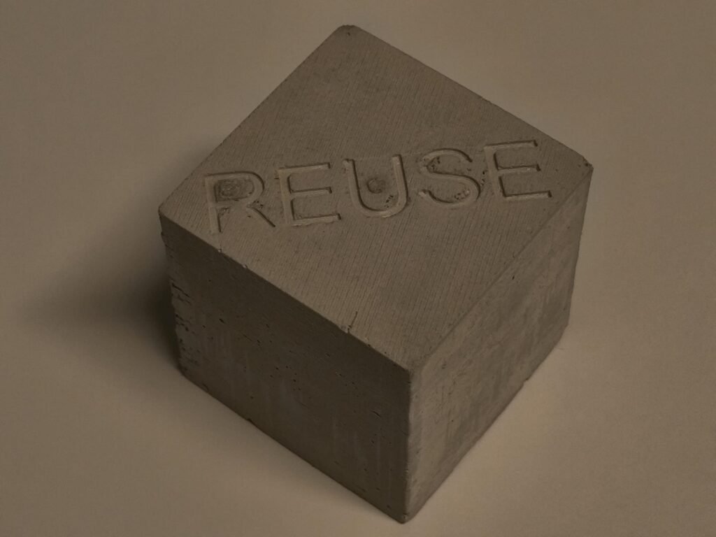Bloc de béton gris portant le mot REUSE gravé en relief.