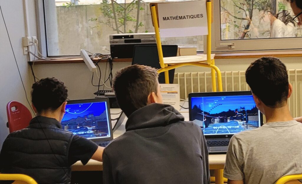 Trois lycéens de dos travaillent devant des ordinateurs portables dans une salle de classe.