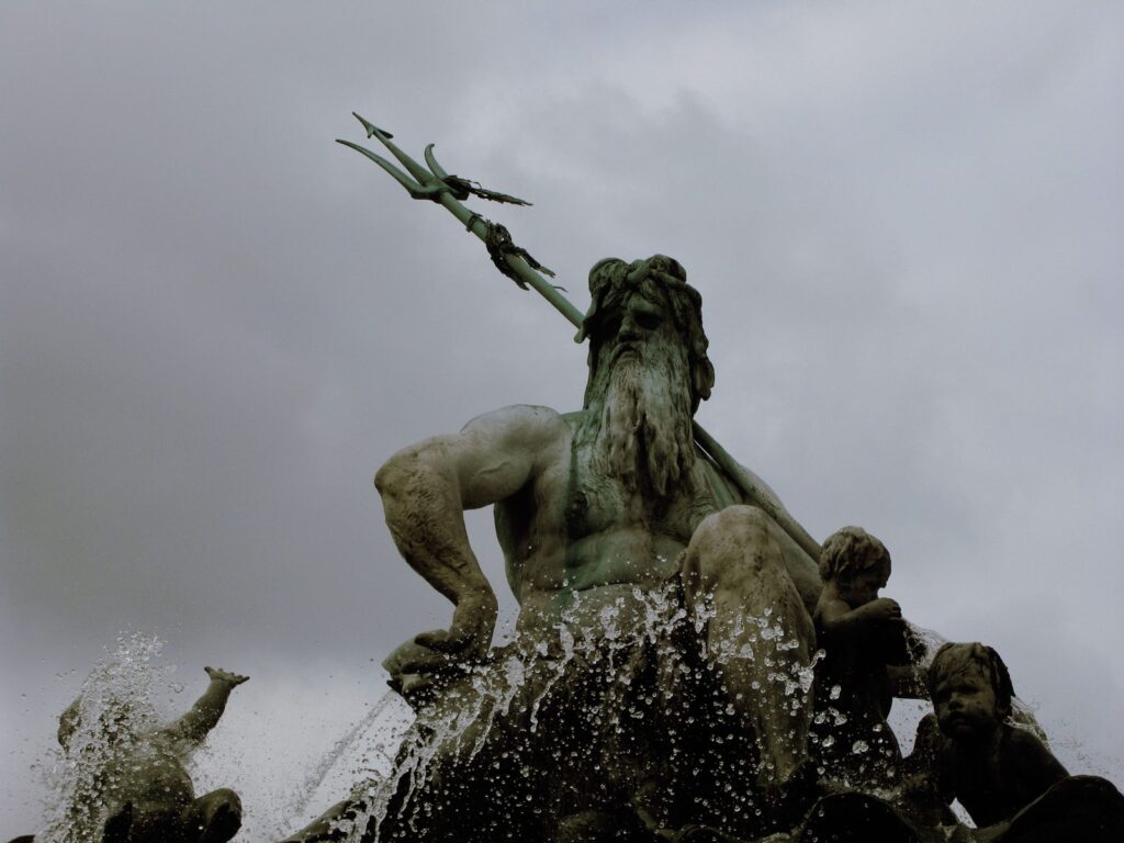 Statue de pierre d'un dieu marin brandissant un trident, dans les embruns.