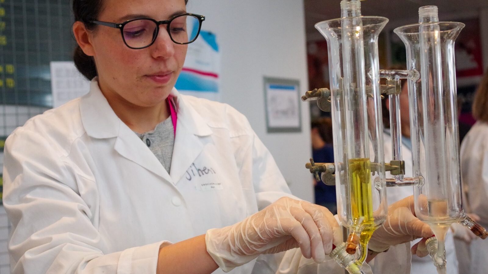 Une jeune chercheuse en blouse ajuste des colonnes de verre sur un montage de laboratoire.