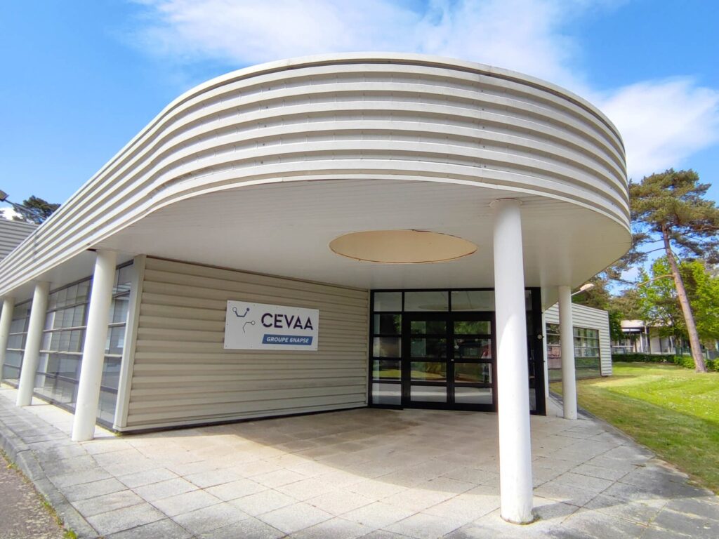 Entrée d'un centre d'essais, auvent blanc soutenu par des piliers.