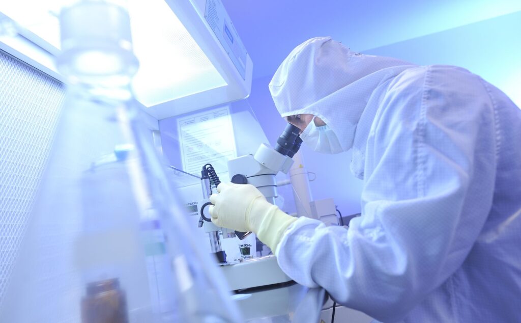 Une personne en combinaison de salle blanche observe un échantillon au microscope.