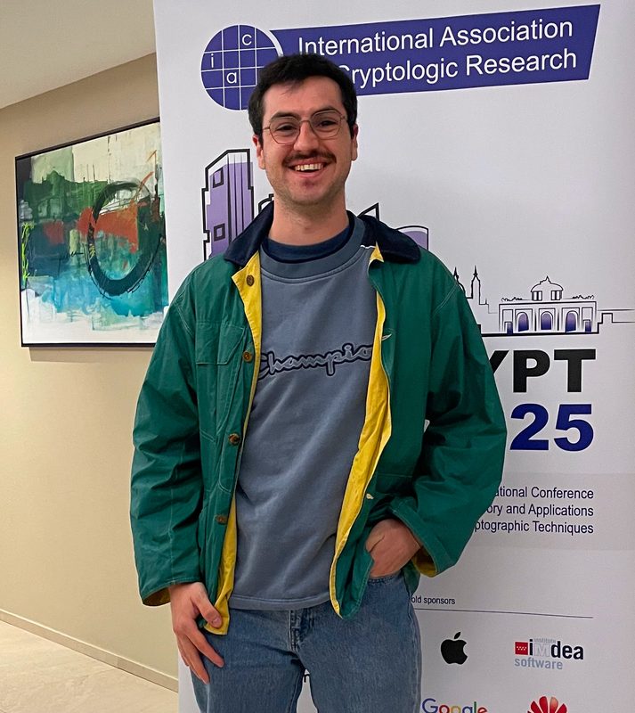 Antoine Douteau, doctorant en cryptographie, devant une affiche de conférence scientifique.