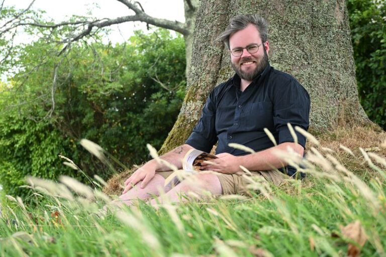 Raphaël Dubois assis dans l'herbe au pied d'un arbre.