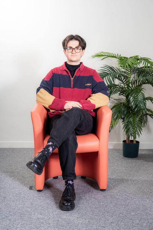 Tom Lebreton, doctorant en philosophie, assis dans un fauteuil orange.