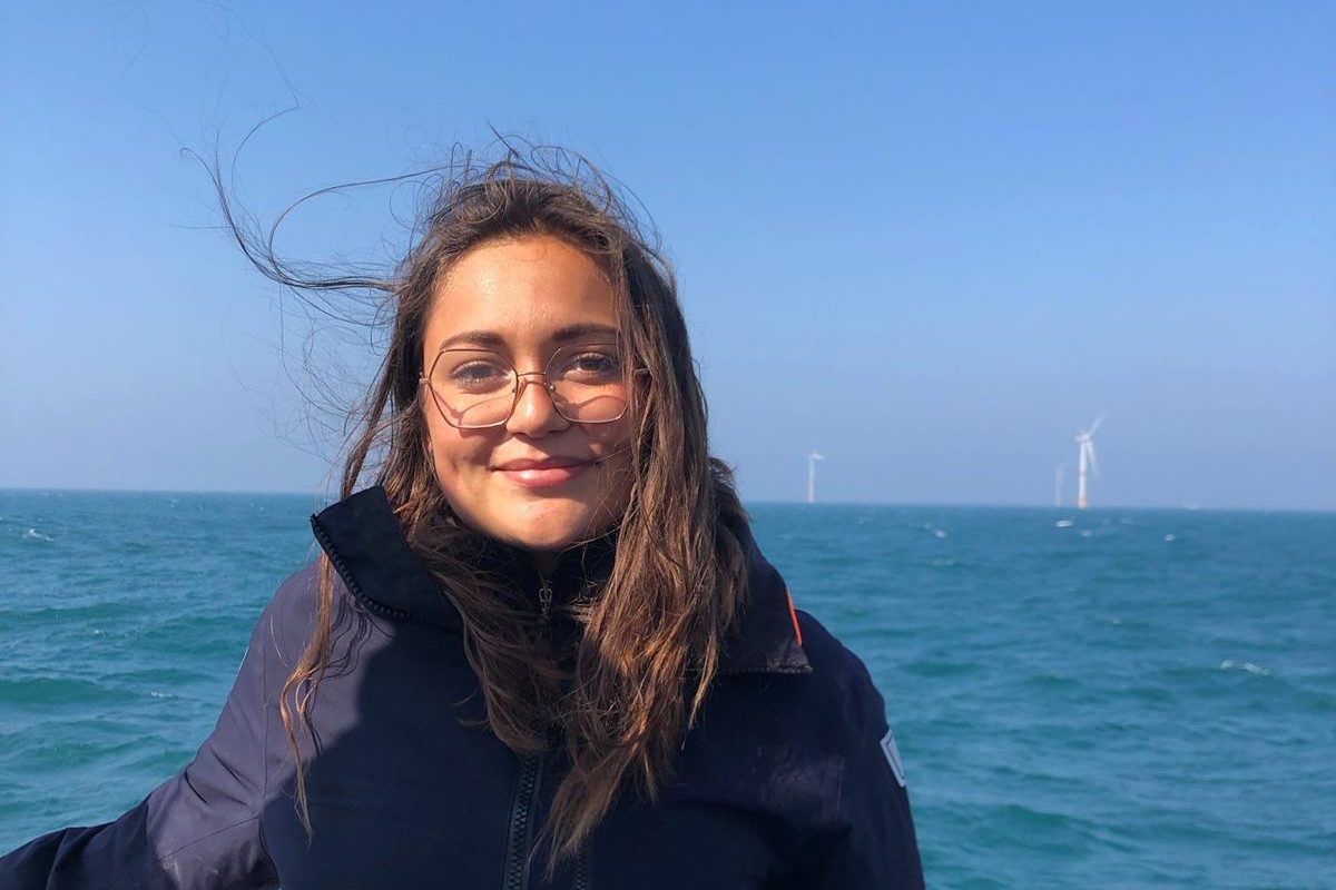 Mathilde Charbonnelle sur le pont d'un bateau, en mer, des éoliennes au loin.